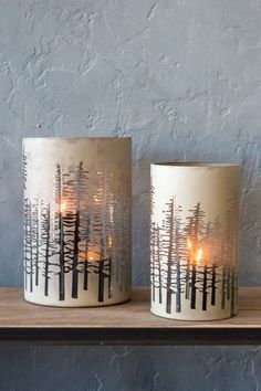 two candles sitting on top of a table next to each other with trees painted on them