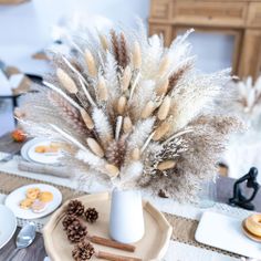 there is a white vase with some dried flowers in it on the dining room table