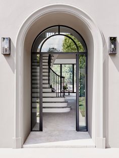 an arched doorway leading into a white house with stairs and windows on either side,