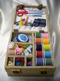 an open wooden box filled with lots of crafting supplies on top of a white sheet