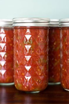 four jars filled with red pickles sitting on top of a wooden table next to each other