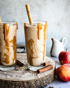 two glasses filled with caramel latte sitting on top of a wooden table next to cinnamon sticks