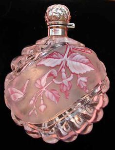 a pink and white glass perfume bottle with floral designs on the top, sitting on a black surface