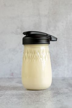 a glass jar with a black lid sitting on top of a white countertop next to a gray wall