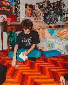 a young man sitting on the floor in front of a bed covered in posters and pictures