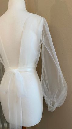 a mannequin wearing a white dress with sheer sleeves and a bow at the waist