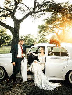 a bride and groom standing in front of an old white car with the door open