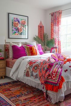 a bed with colorful blankets and pillows in a bedroom next to a window filled with potted plants