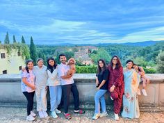 a group of people standing next to each other on top of a stone wall with trees in the background