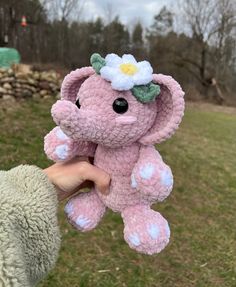 a pink crocheted elephant with a flower on its head is being held by someone