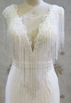 a white dress with fringes and beads on the shoulders is displayed in front of a mannequin's head