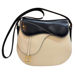 This beautiful vintage GUCCI two-toned saddle bag is crafted of smooth calfskin leather in off-white and navy featuring gold toned hardware. Front magnetic snap closure decorated with a stirrup charm opens to a beige leather interior with a zippered pocket. A very rare quiet luxury piece from The House of Gucci. Made in Italy. Measures approximately 9 x 8.5 x 3 inches Strap drop 20 inches at its longest. Comes with dust bag. Condition - Very good vintage condition with minor signs of wear Outsid Vintage Gucci Bag, The House Of Gucci, Cream Purse, Gucci Vintage Bag, Gucci Outfits, Gucci Monogram, Gucci Shoulder Bag, Black Leather Crossbody Bag, Quiet Luxury