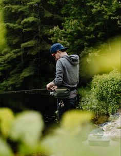 a man standing in the water while holding onto a fishing rod and wearing a hat