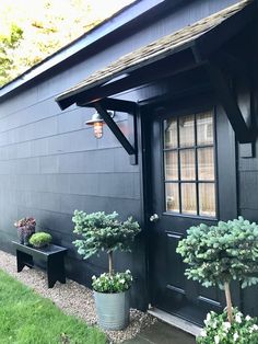 two potted plants are sitting in front of a black door and window on the side of a house