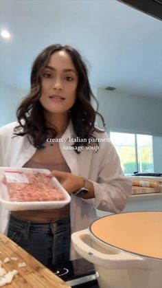 a woman standing in front of a counter holding a container with food inside of it