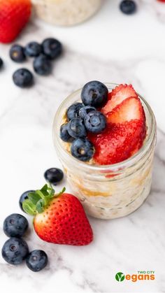 a glass jar filled with oatmeal and strawberries next to blueberries