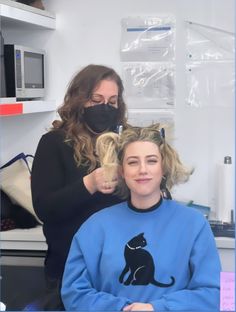 a woman is getting her hair cut by a lady in a blue sweatshirt and black face mask