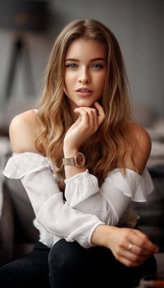 a beautiful woman sitting on top of a couch wearing a white shirt and black pants