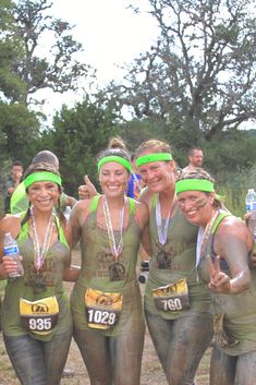 some women in mud paint are posing for a photo with their medals and water bottles