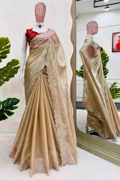 Step into elegance with this exquisite dark ivory shimmery tissue silk saree, crafted from a super soft shine fabric that drapes beautifully and feels luxurious against the skin. The saree's subtle shimmer adds a refined glow, making it the perfect choice for weddings, festive events, and special occasions. Paired with a vibrant red embroidered blouse adorned with delicate white floral patterns, this saree creates a stunning visual contrast that enhances your overall look. The intricate sequin embellishments along the saree's scalloped border showcase fine craftsmanship, blending traditional aesthetics with a contemporary touch. The soft texture ensures comfort while exuding opulence, making it a versatile addition to your ethnic wardrobe. Key Features: * Saree Color: Dark ivory with a shi Gold Raw Silk Shawl With Traditional Drape, Elegant Gold Embroidered Saree Fabric, Traditional Drape Raw Silk Embroidered Fabric In Gold, Gold Pre-draped Saree With Embroidered Border In Raw Silk, Gold Embroidered Saree Fabric With Border, Dark Red Blouse, White Sari, Open Blouse, Tissue Silk Saree