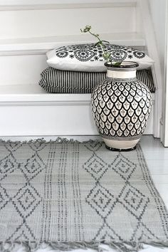 a black and white vase sitting on top of a rug next to a window sill