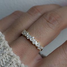 a woman's hand wearing a gold ring with three stones on it and a white sweater in the background