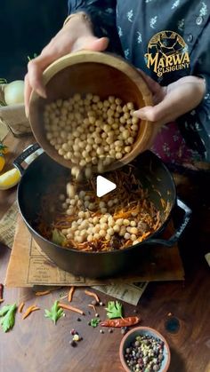 a person pouring beans into a pot on top of a wooden table next to other food items