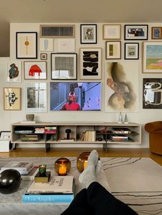 a person's feet resting on a coffee table in front of a wall full of pictures