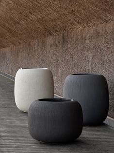 three black and white vases sitting next to each other on a wooden floor in front of a wall