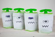 four green and white halloween treat bags with faces drawn on them, sitting on a wooden table