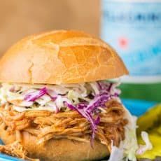 a pulled pork sandwich with coleslaw and pickles on a blue plate next to a banana