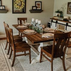 a dining room table set for four with place settings on the wall and pictures above it