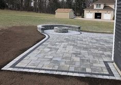 a brick patio in the middle of a yard with a fire pit on one side