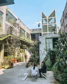 two people sitting on chairs in an open courtyard area with plants and potted trees