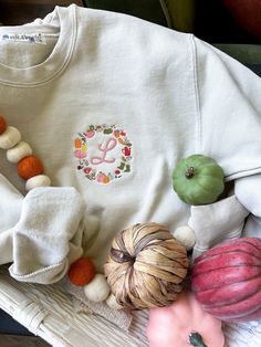 cozy up for fall in the sweetest embroidered autumn harvest wreath sweatshirt featuring mini pumpkins, pots of tea, and boots for mucking about. personalized in the middle with your initial in a double satin chain stitch in your thread color of choice ::THE DETAILS:: - machine embroidered along left side chest - 1 character limit for monogram in font as shown - gildan sweatshirt & t-shirt, please review size chart in photos before ordering - machine washable x tumble dry low ::PLEASE NOTE:: - due to the customized nature of this item, refunds or returns cannot be accepted - please ask any questions before ordering CUSTOM ORDERS WELCOME! if you don't see what you're looking for - message me and we can work together to make your perfect sweatshirt! Monogram Sweatshirt, Harvest Wreath, Side Chest, Gildan Sweatshirt, Monogram Wreath, Autumn Harvest, Mini Pumpkins, Gildan Sweatshirts, Fall Harvest