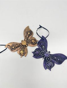 two purple and gold butterfly brooches on a white background, one with an intricate design