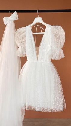 two white dresses hanging on a rack in front of a pink wall and one is wearing a veil