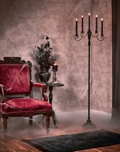 a red chair sitting on top of a wooden floor next to a tall candle holder