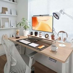 a computer monitor sitting on top of a wooden desk next to a white chair and potted plant