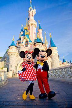 two mickey and minnie mouse standing in front of a castle at disney world with their arms around each other