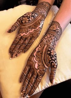 two hands with henna designs on them sitting on a cushion in front of a woman's arm