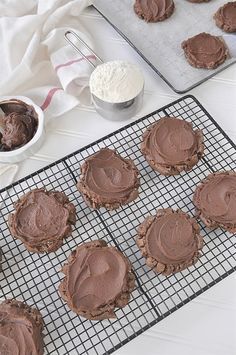 chocolate cookies with frosting on a cooling rack next to baking utensils and bowls