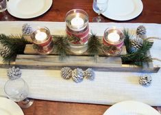 a candle holder with pine cones and candles on top of a wooden board that is sitting on a dining room table