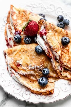 pancakes with blueberries, strawberries and powdered sugar are on a white plate