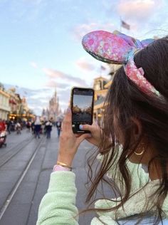 a woman taking a photo with her cell phone in front of the disney world main street