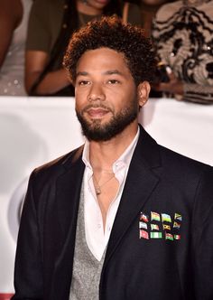 a man with curly hair wearing a black suit and white shirt, standing in front of a crowd