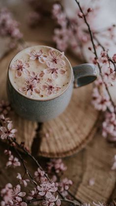 a cup of hot chocolate with pink flowers on the side sitting on top of a piece of wood