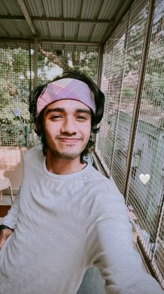 a man wearing a pink bandana standing in front of a bird cage with his eyes closed