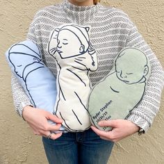 a woman is holding two pillows in her hands, one with a sleeping baby on it