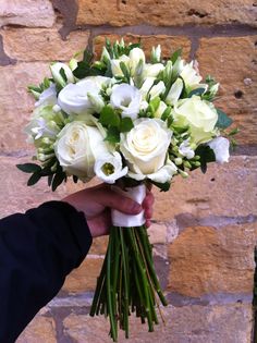 a person holding a bouquet of white flowers in front of a brick wall with green foliage